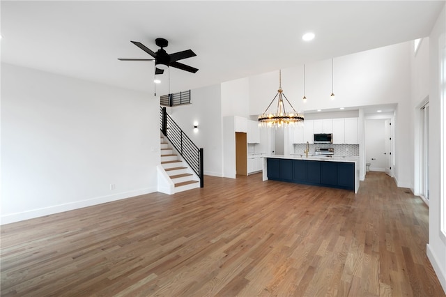 kitchen with decorative backsplash, light hardwood / wood-style floors, white cabinetry, pendant lighting, and a kitchen island with sink