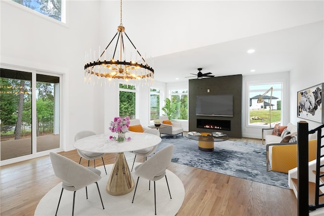 dining space with light hardwood / wood-style flooring, a large fireplace, a high ceiling, and ceiling fan with notable chandelier