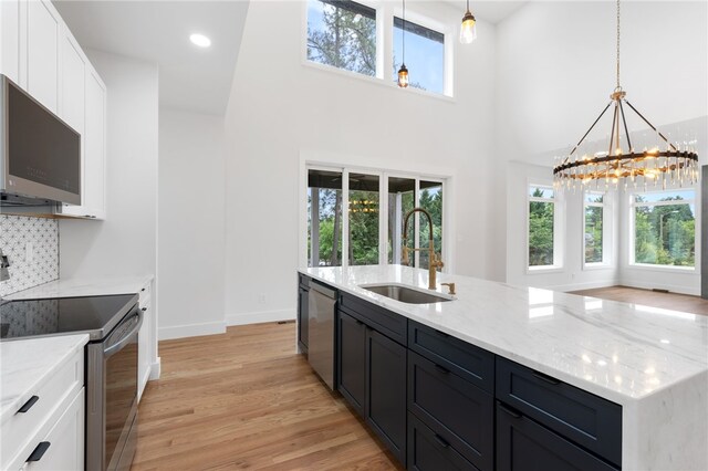 kitchen with appliances with stainless steel finishes, white cabinets, light wood-type flooring, decorative light fixtures, and sink