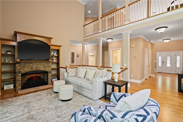 living room featuring light hardwood / wood-style flooring, decorative columns, a high ceiling, a fireplace, and crown molding