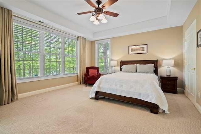 bedroom with ceiling fan, light colored carpet, and a raised ceiling