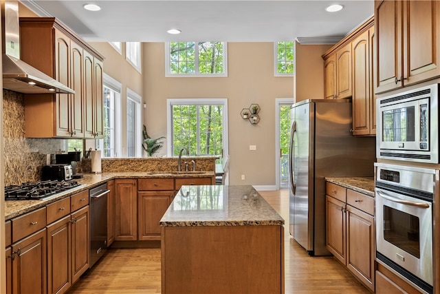 kitchen with stainless steel appliances, wall chimney exhaust hood, sink, and light hardwood / wood-style flooring