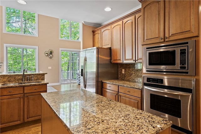 kitchen featuring light stone countertops, stainless steel appliances, a kitchen island, and sink