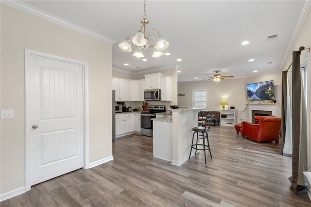 kitchen featuring light wood-type flooring, appliances with stainless steel finishes, hanging light fixtures, and white cabinetry