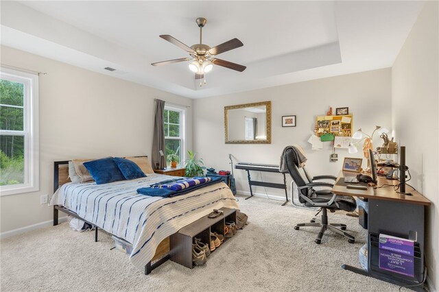 carpeted bedroom with ceiling fan and a raised ceiling