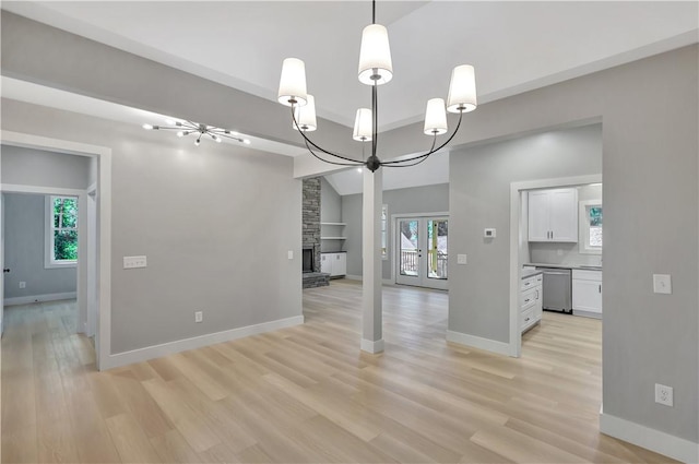 unfurnished dining area featuring french doors, an inviting chandelier, lofted ceiling, a fireplace, and light wood-type flooring