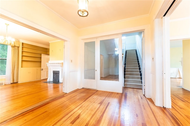 unfurnished living room featuring built in shelves, hardwood / wood-style flooring, ornamental molding, and a high end fireplace