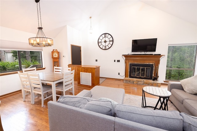 living room featuring light wood-type flooring, a stone fireplace, a chandelier, and high vaulted ceiling