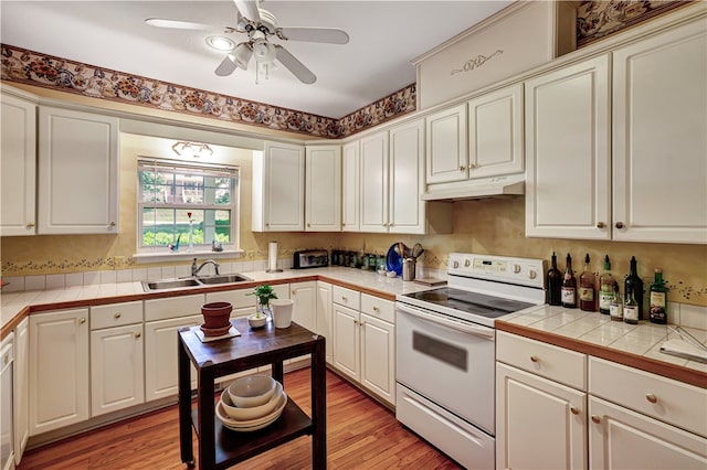 kitchen with ceiling fan, sink, light hardwood / wood-style flooring, tile countertops, and electric stove