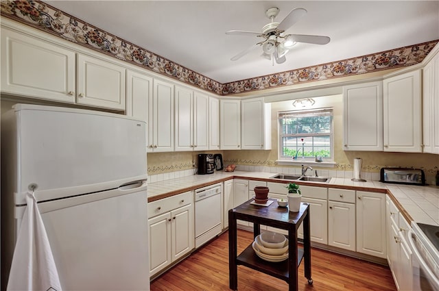 kitchen featuring ceiling fan, sink, white appliances, light hardwood / wood-style flooring, and tile counters