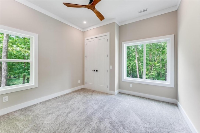 carpeted empty room featuring visible vents, crown molding, baseboards, and ceiling fan