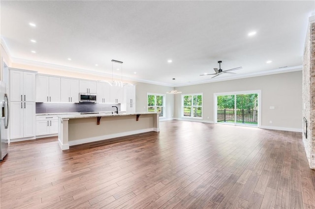 kitchen featuring white cabinetry, crown molding, a center island with sink, pendant lighting, and stainless steel appliances