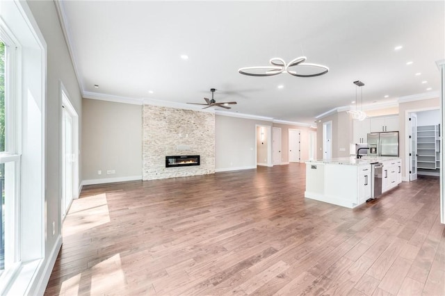 unfurnished living room featuring baseboards, ceiling fan, ornamental molding, wood finished floors, and a stone fireplace