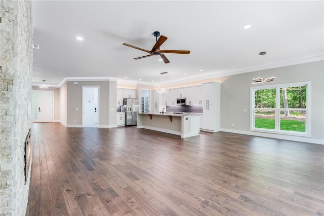 unfurnished living room with dark hardwood / wood-style flooring, sink, ceiling fan with notable chandelier, and ornamental molding