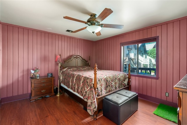 bedroom featuring wood-type flooring, wood walls, and ceiling fan