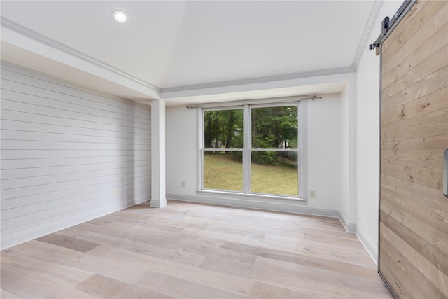 spare room with wooden walls, light hardwood / wood-style floors, crown molding, and a barn door