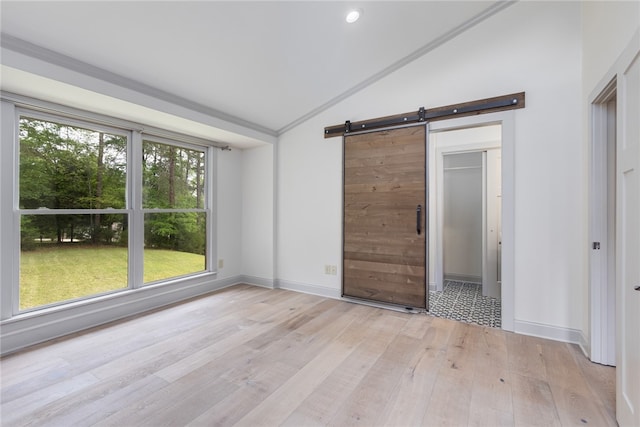 empty room with a barn door, lofted ceiling, and light hardwood / wood-style floors