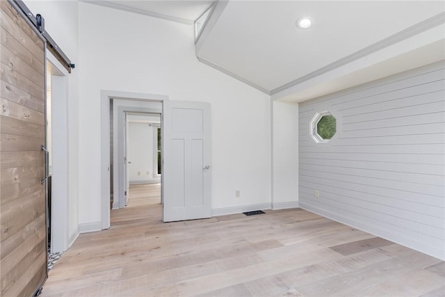 spare room featuring a barn door, light wood-type flooring, wood walls, and baseboards