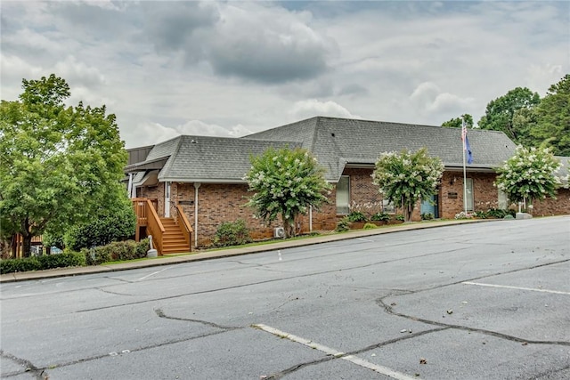 exterior space featuring uncovered parking, brick siding, and roof with shingles
