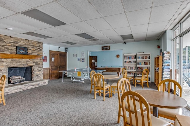 dining area with a paneled ceiling, a stone fireplace, and carpet