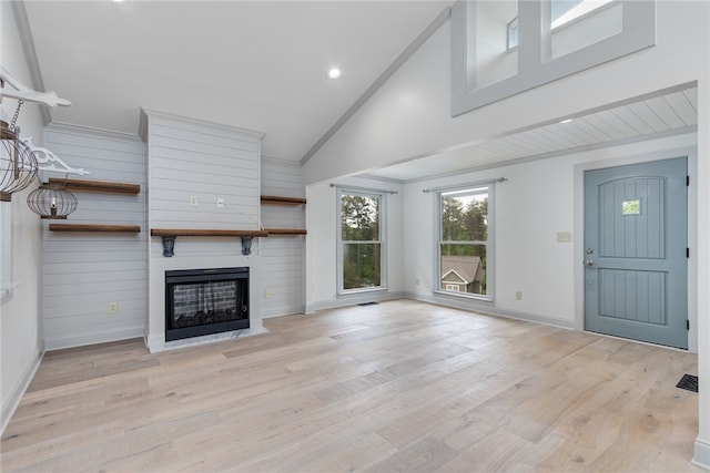 unfurnished living room featuring light wood-type flooring, wooden walls, a large fireplace, and high vaulted ceiling