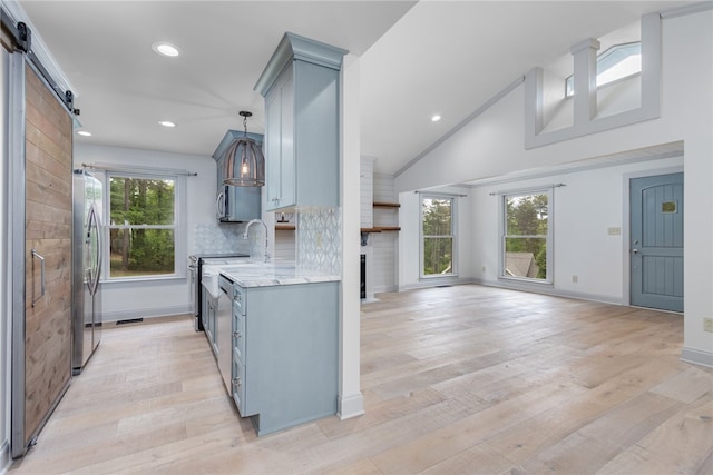 kitchen featuring light stone counters, stainless steel fridge, tasteful backsplash, light wood-type flooring, and a barn door