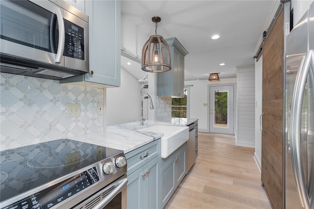 kitchen with pendant lighting, sink, stainless steel appliances, light wood-type flooring, and a barn door