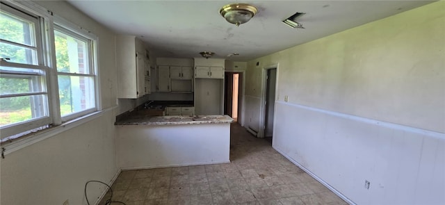 kitchen with light tile patterned flooring, sink, kitchen peninsula, and white cabinets