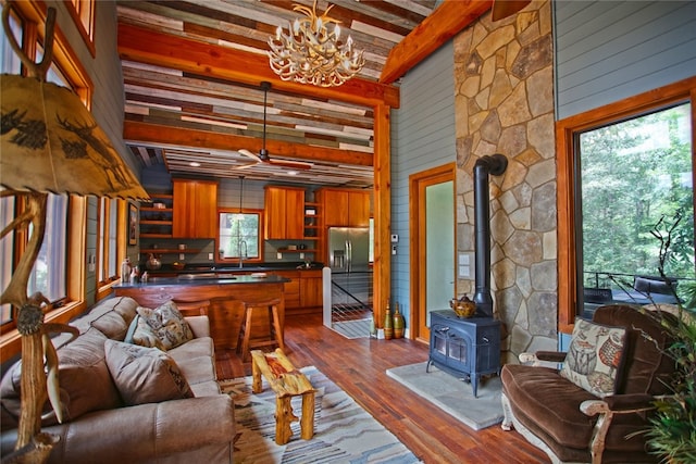 living room with a wood stove, ceiling fan with notable chandelier, sink, beam ceiling, and dark hardwood / wood-style floors