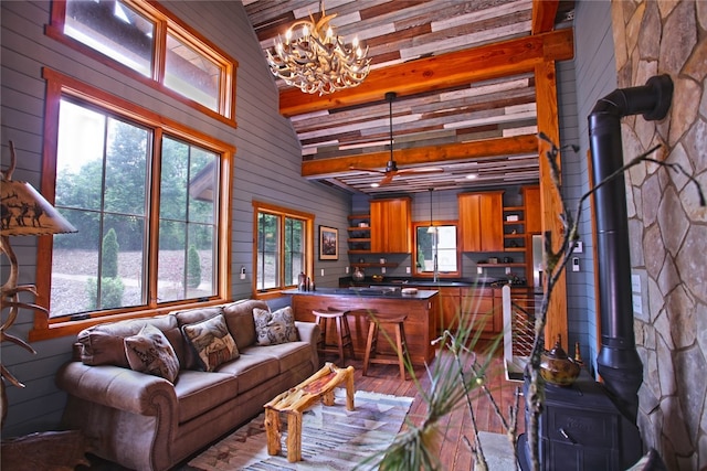 living room with beamed ceiling, ceiling fan with notable chandelier, a healthy amount of sunlight, and a wood stove