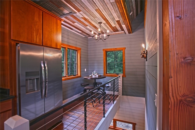 kitchen with stainless steel fridge, wood walls, a notable chandelier, and plenty of natural light