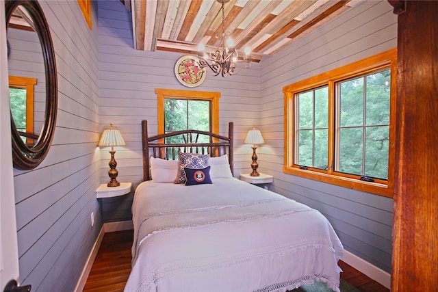 bedroom with an inviting chandelier, dark wood-type flooring, and wooden walls