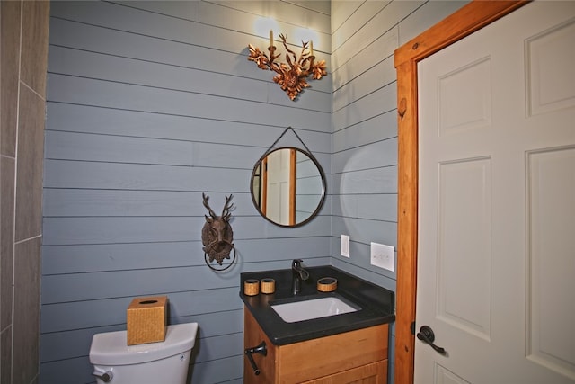 bathroom with vanity, toilet, and wood walls