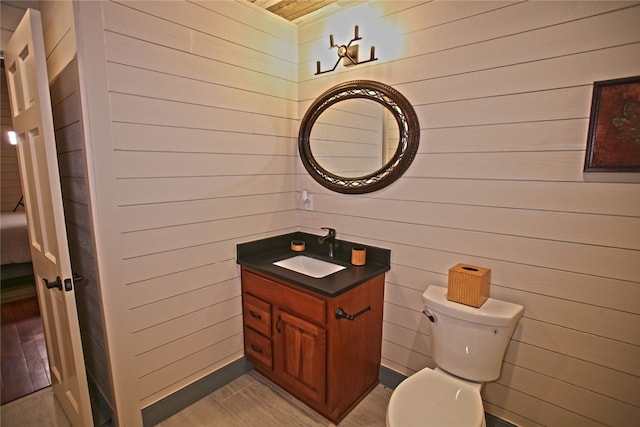 bathroom featuring wooden walls, vanity, tile patterned flooring, and toilet