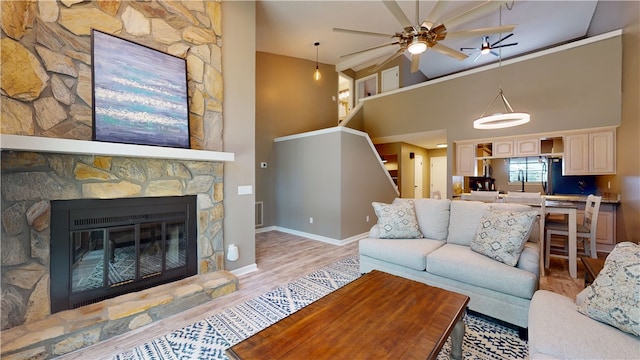 living room featuring a fireplace, a high ceiling, light wood-type flooring, and ceiling fan