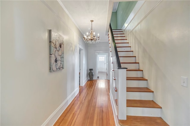 stairs featuring hardwood / wood-style flooring, crown molding, and a notable chandelier