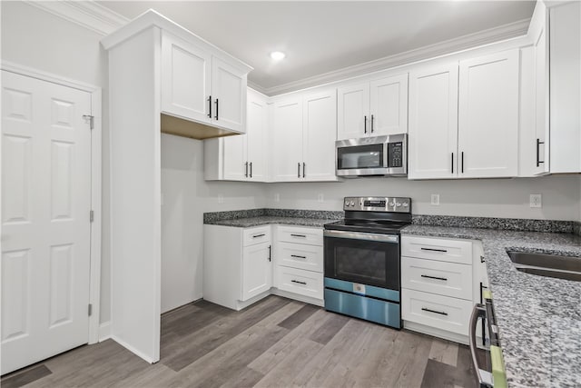 kitchen with white cabinetry, ornamental molding, light stone countertops, light hardwood / wood-style floors, and appliances with stainless steel finishes