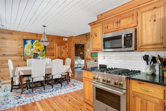 kitchen featuring wooden walls, pendant lighting, stainless steel appliances, light hardwood / wood-style floors, and decorative backsplash