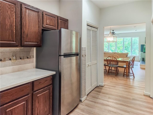 kitchen featuring stainless steel refrigerator, ceiling fan, decorative backsplash, dark brown cabinets, and light wood-type flooring