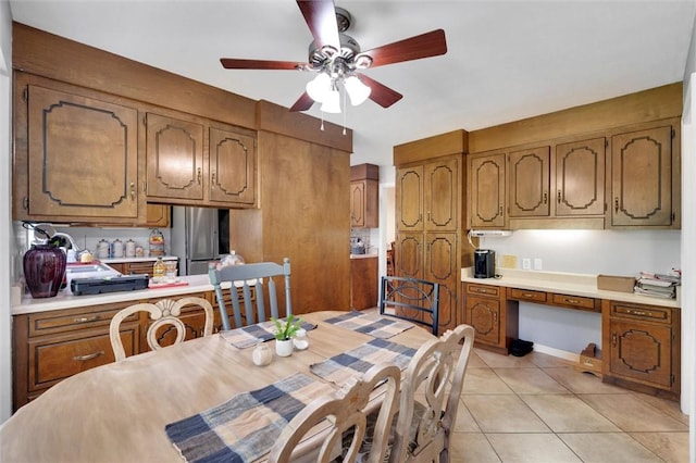 dining room with built in desk, light tile patterned floors, and ceiling fan