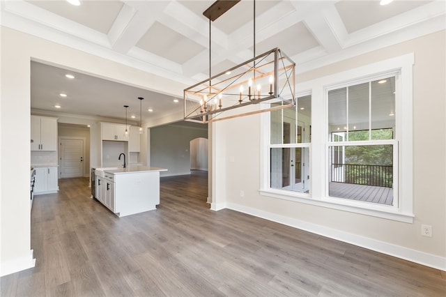 kitchen featuring white cabinets, pendant lighting, an island with sink, coffered ceiling, and hardwood / wood-style flooring