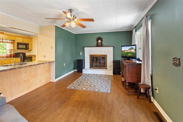 living room with ceiling fan, sink, hardwood / wood-style flooring, a fireplace, and ornamental molding