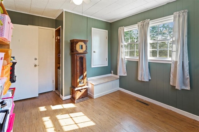 spare room featuring wood walls, ornamental molding, and light wood-type flooring