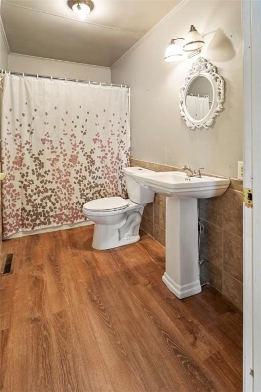 bathroom with hardwood / wood-style flooring, toilet, ornamental molding, and tile walls