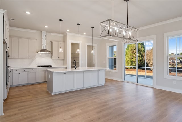 kitchen featuring pendant lighting, light hardwood / wood-style floors, backsplash, a kitchen island with sink, and wall chimney exhaust hood