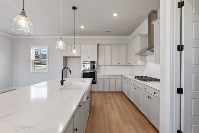 kitchen featuring light hardwood / wood-style floors, decorative light fixtures, appliances with stainless steel finishes, and wall chimney range hood