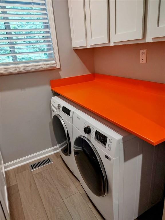 clothes washing area with cabinets, washer and clothes dryer, and light hardwood / wood-style flooring