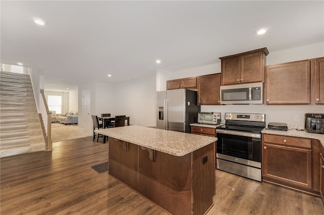 kitchen featuring appliances with stainless steel finishes, light stone countertops, a breakfast bar area, dark hardwood / wood-style flooring, and a center island