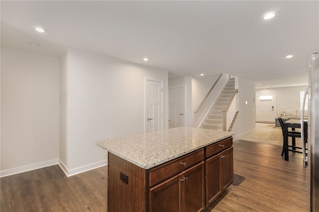 kitchen with dark brown cabinets, light stone counters, a kitchen island, and dark hardwood / wood-style flooring