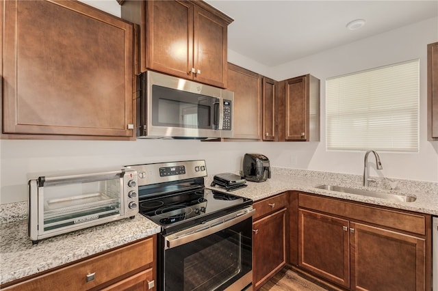 kitchen with appliances with stainless steel finishes, light stone countertops, sink, and wood-type flooring